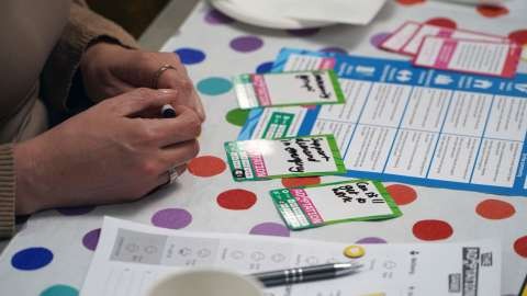 A close up of people playing the The Adaptation Game, showing the board game, cards and game pieces. 